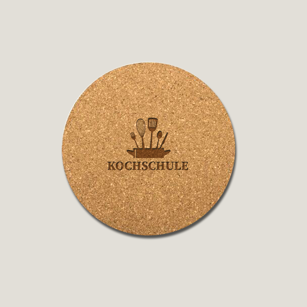 Runder Korkuntersetzer mit graviertem Motiv aus Küchenutensilien und dem Schriftzug „KOCHSCHULE“ auf hellem Hintergrund.