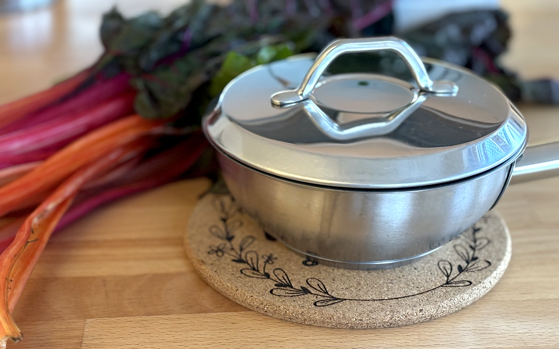 Kochtopf mit Deckel auf rundem Korkuntersetzer mit graviertem floralem Motiv.