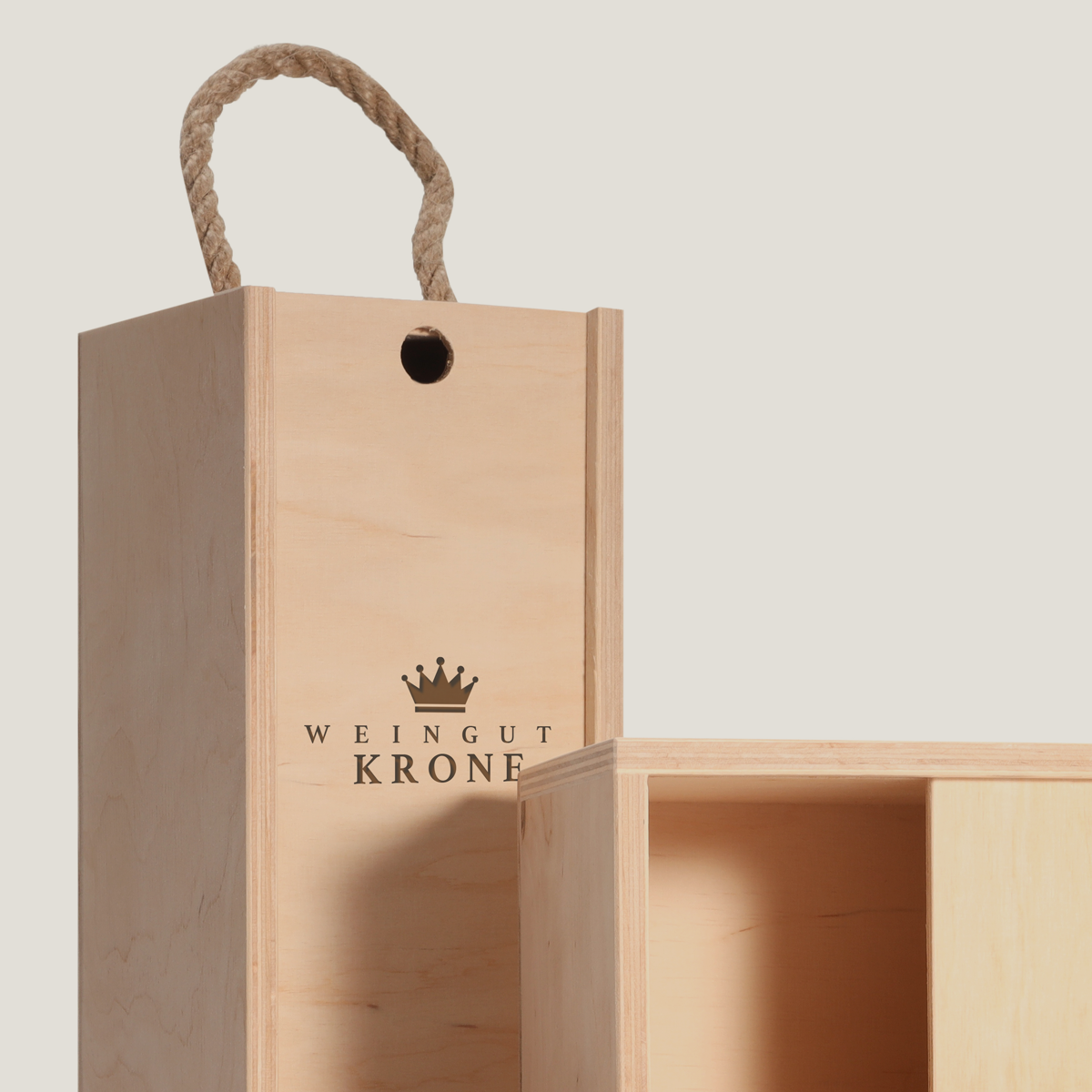 Holz-Weinkiste mit Schiebedeckel und Tragegriff aus Seil, mit Logo "Weingut Krone" graviert, teilweise geöffnet, gefüllt mit Holzwolle.